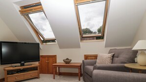 Een woonkamer met een flatscreen televisie, houten meubels, een bank en twee dakramen.