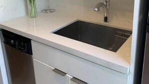 Une cuisine dotée d’un plan de travail blanc, d’un évier en acier inoxydable et d’un lave-vaisselle.