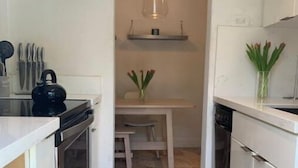 Une cuisine étroite avec des meubles blancs, une bouilloire noire et un luminaire suspendu.