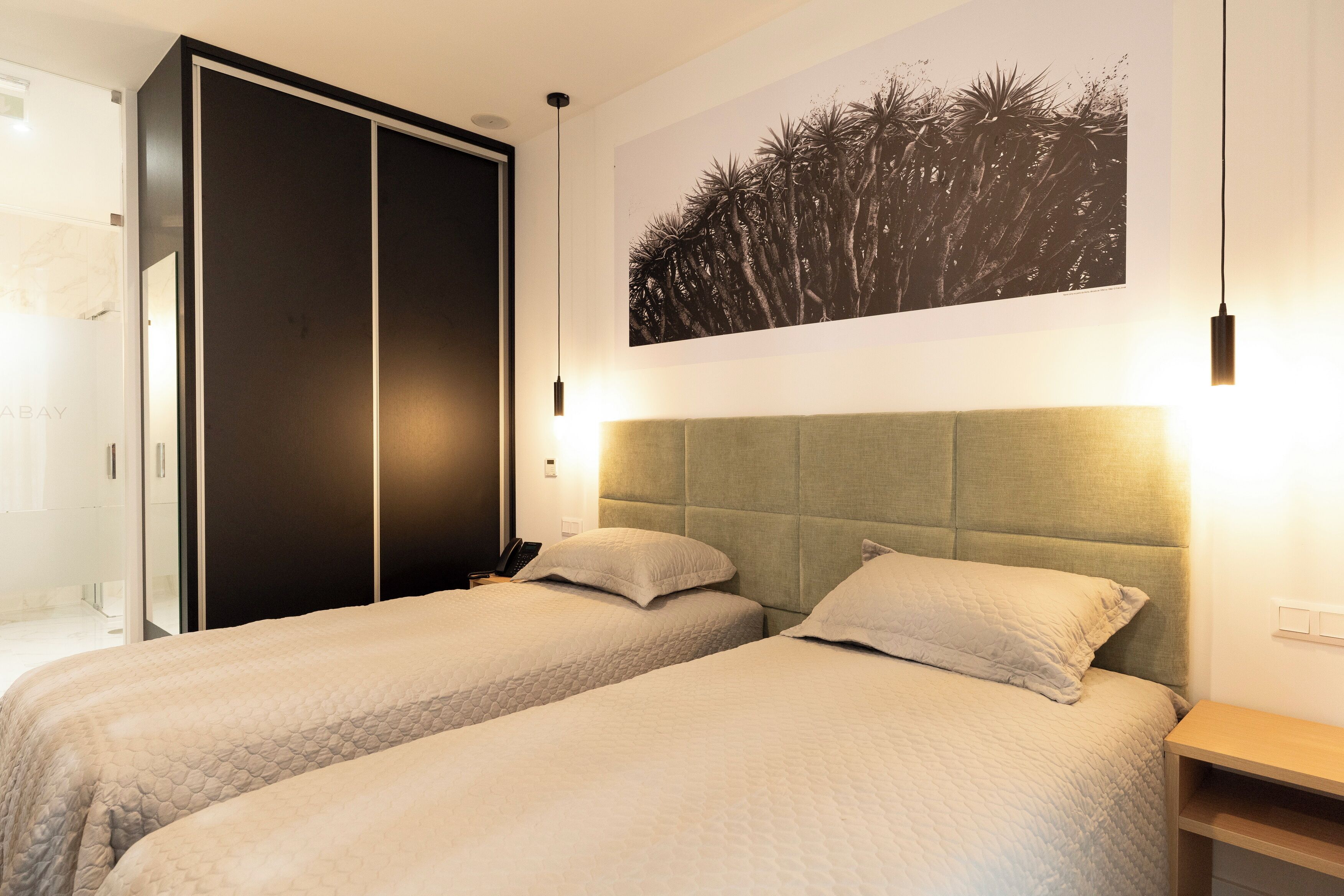 A hotel room with two beds, a wardrobe, a headboard, a bedside table, and a wall-mounted artwork.