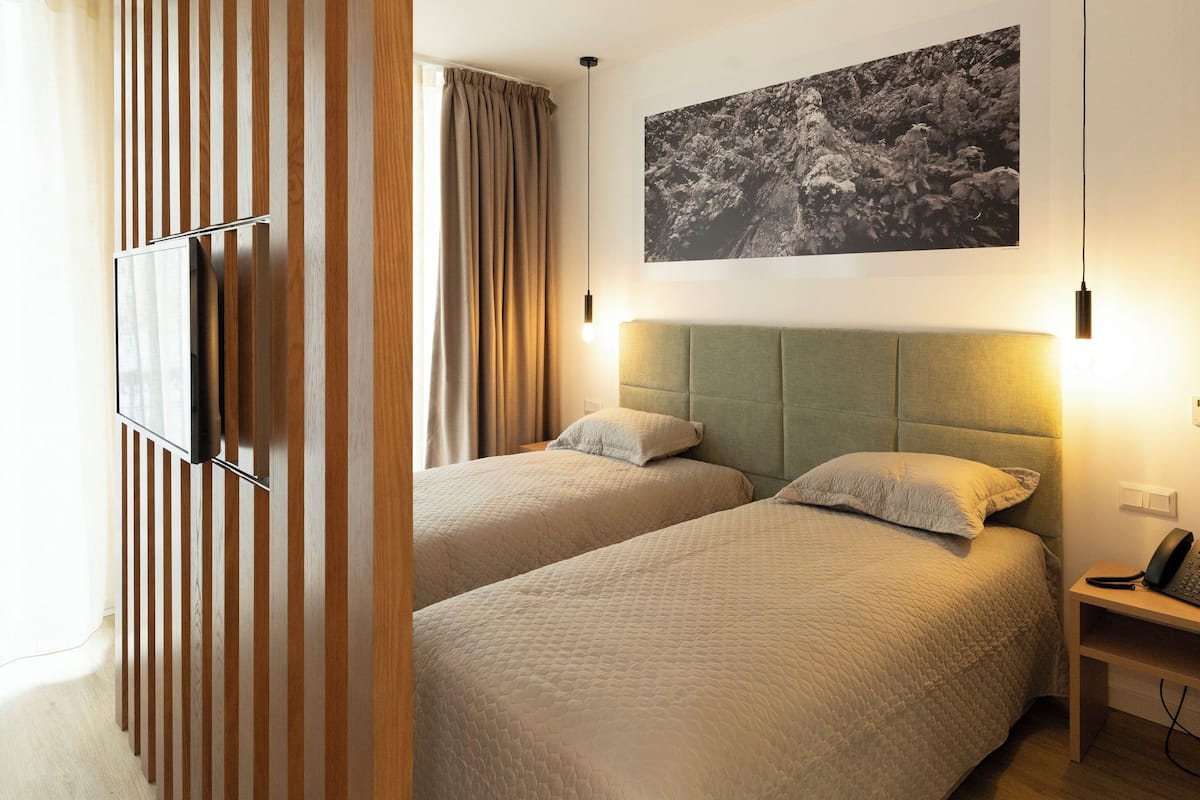 A hotel room with two beds, a mounted TV, a bedside table with a phone, and a wall-mounted artwork.