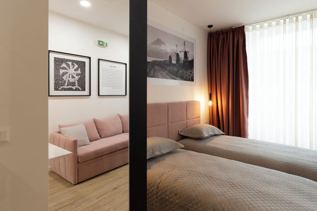 A hotel room with a bed, a sofa, and two framed pictures on the wall.