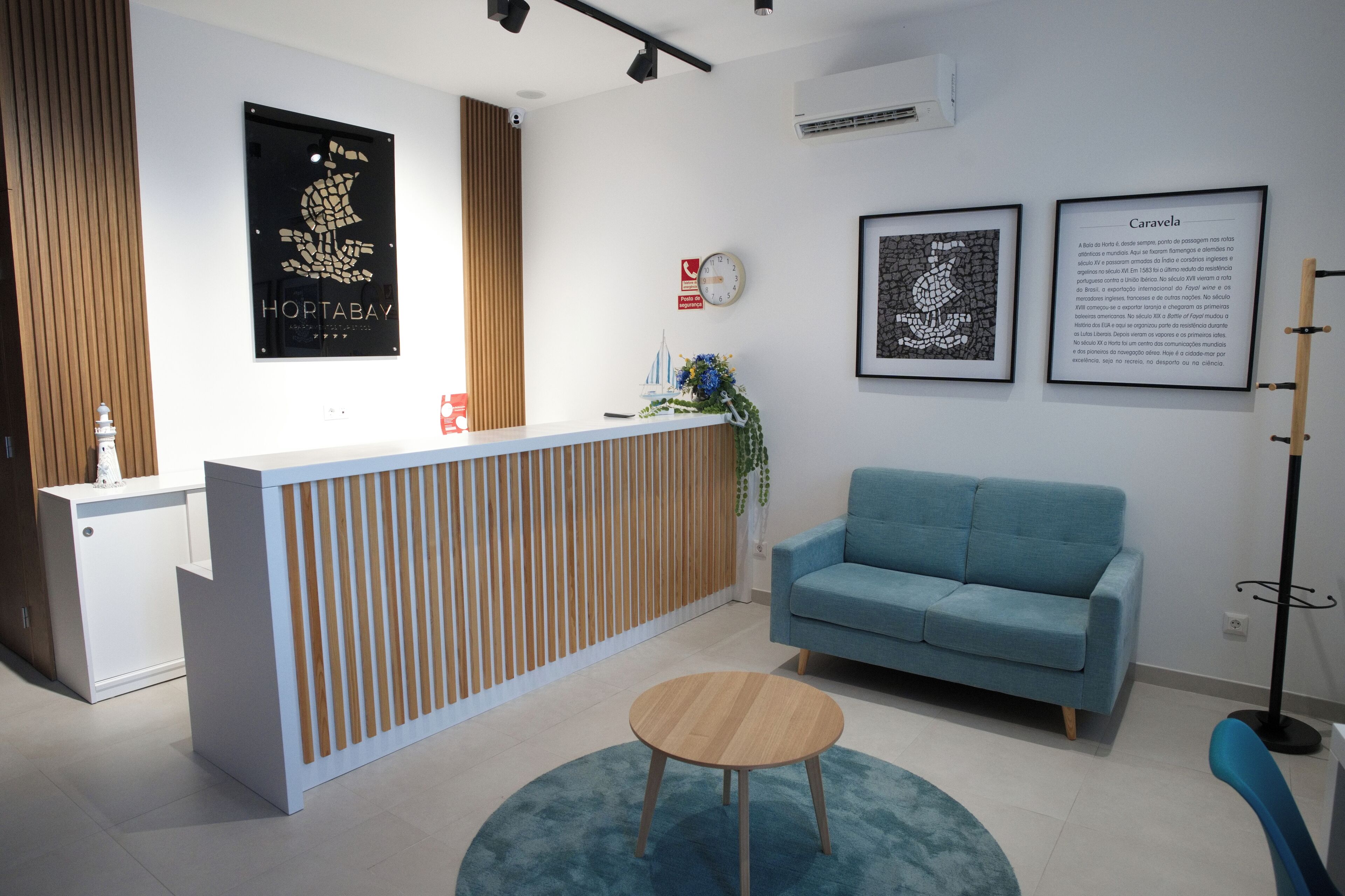 A reception area with a wooden reception desk, a blue sofa, a round wooden table, and framed informational posters on the wall.