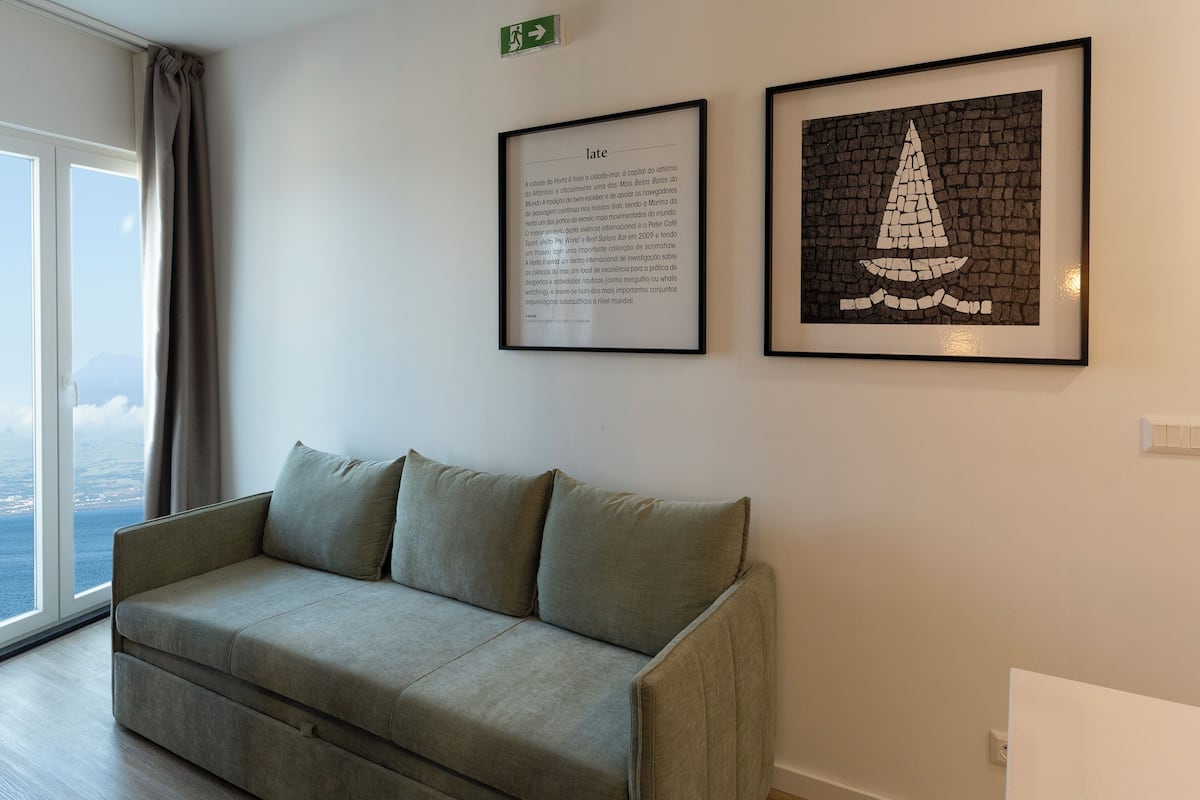 A room with a grey sofa, a framed text on the wall, and a framed artwork depicting a sailboat.