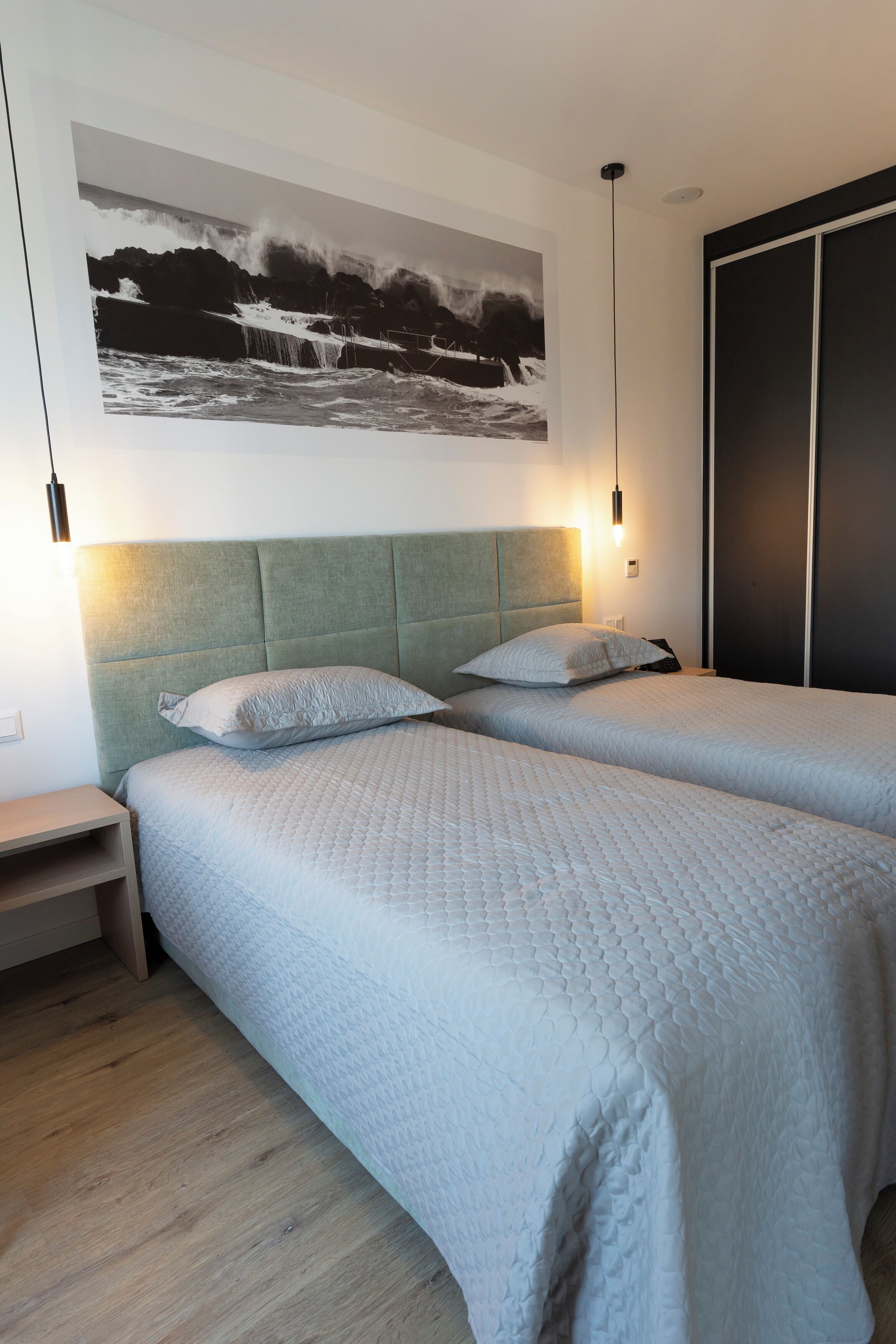 A bedroom with two beds, a headboard, a bedside table, a nightstand, a wall-mounted artwork, and a wardrobe.