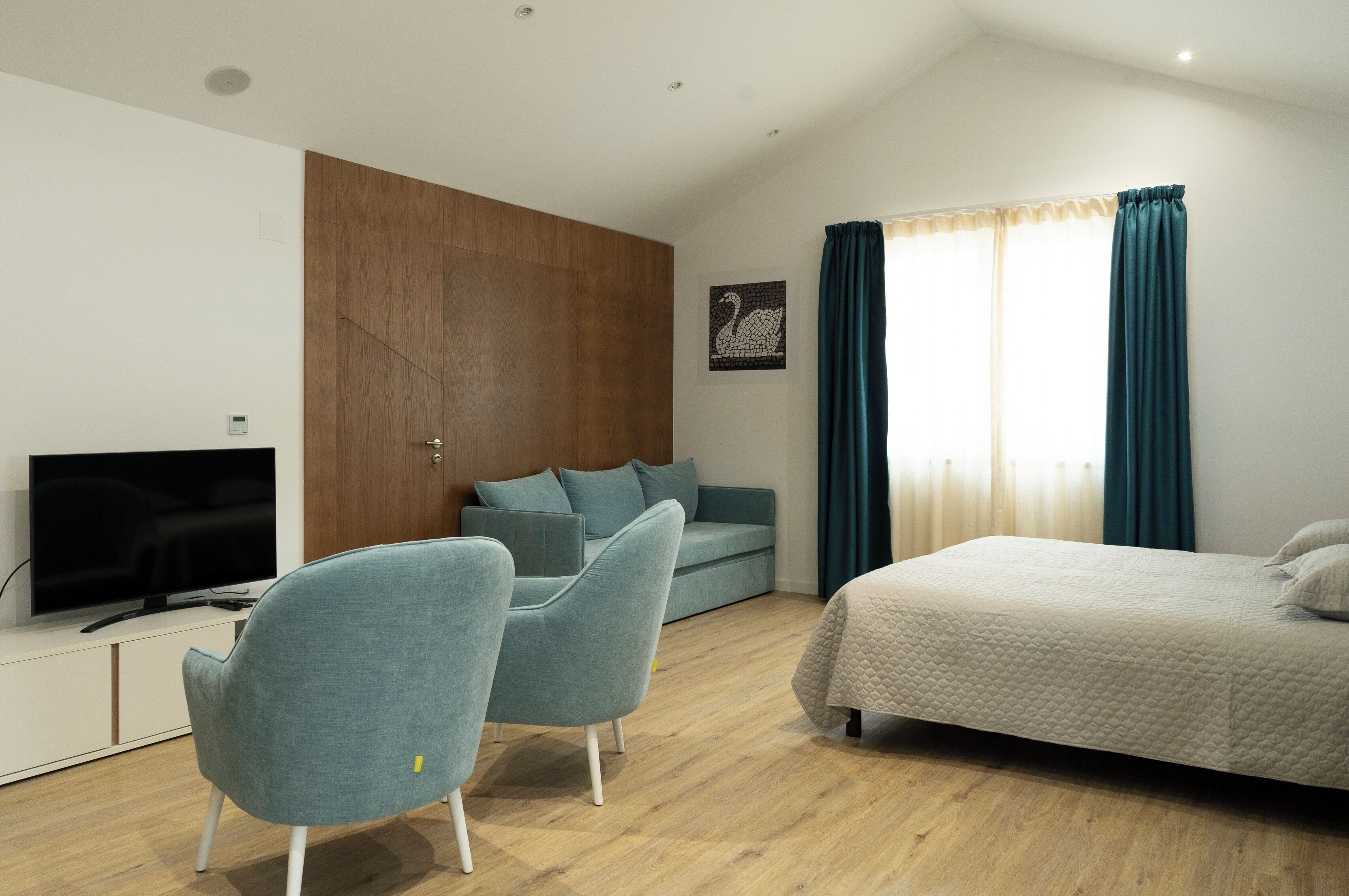 A modern bedroom with a bed, two sofas, a TV, and a wooden panel wall.