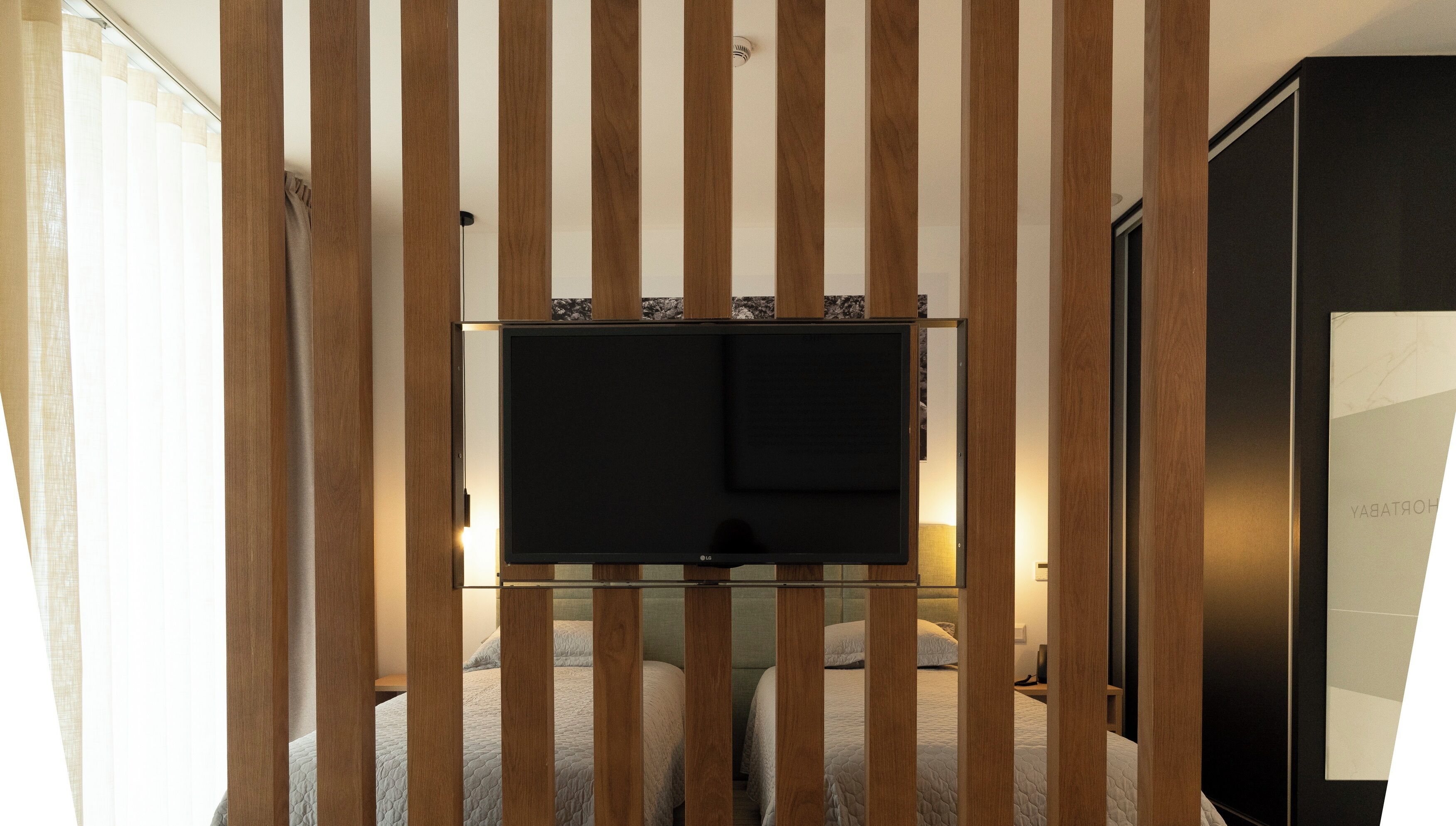 A bedroom with a TV mounted on a wooden panel wall, a bed with a quilted cover, and a wardrobe.