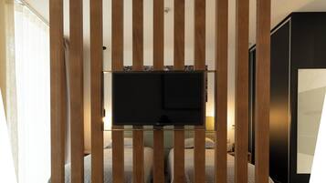 A bedroom with a TV mounted on a wooden panel wall, a bed with a quilted cover, and a wardrobe.