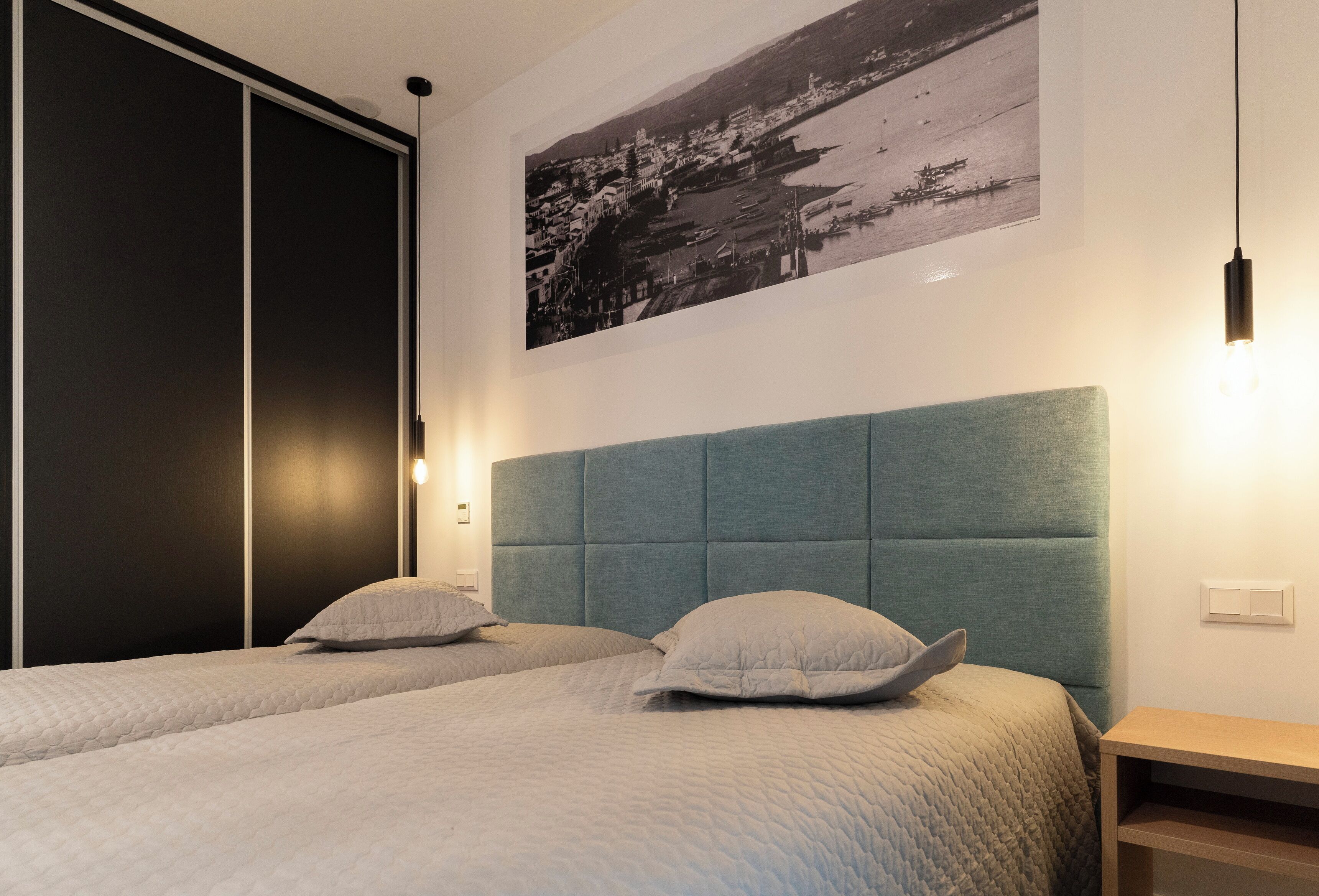 A bedroom with two beds, a large window, and a wall-mounted picture.