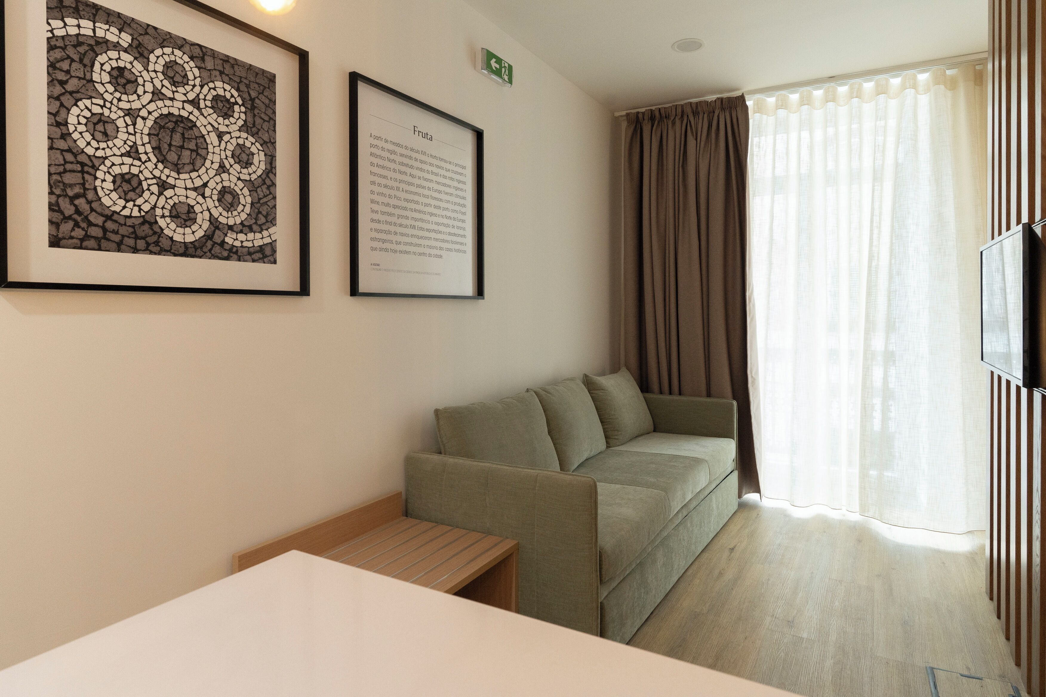 A room with a green sofa, a framed picture on the wall, a small table, and a TV on the right.