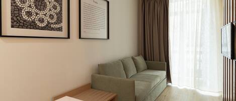 A room with a green sofa, a framed picture on the wall, a small table, and a TV on the right.