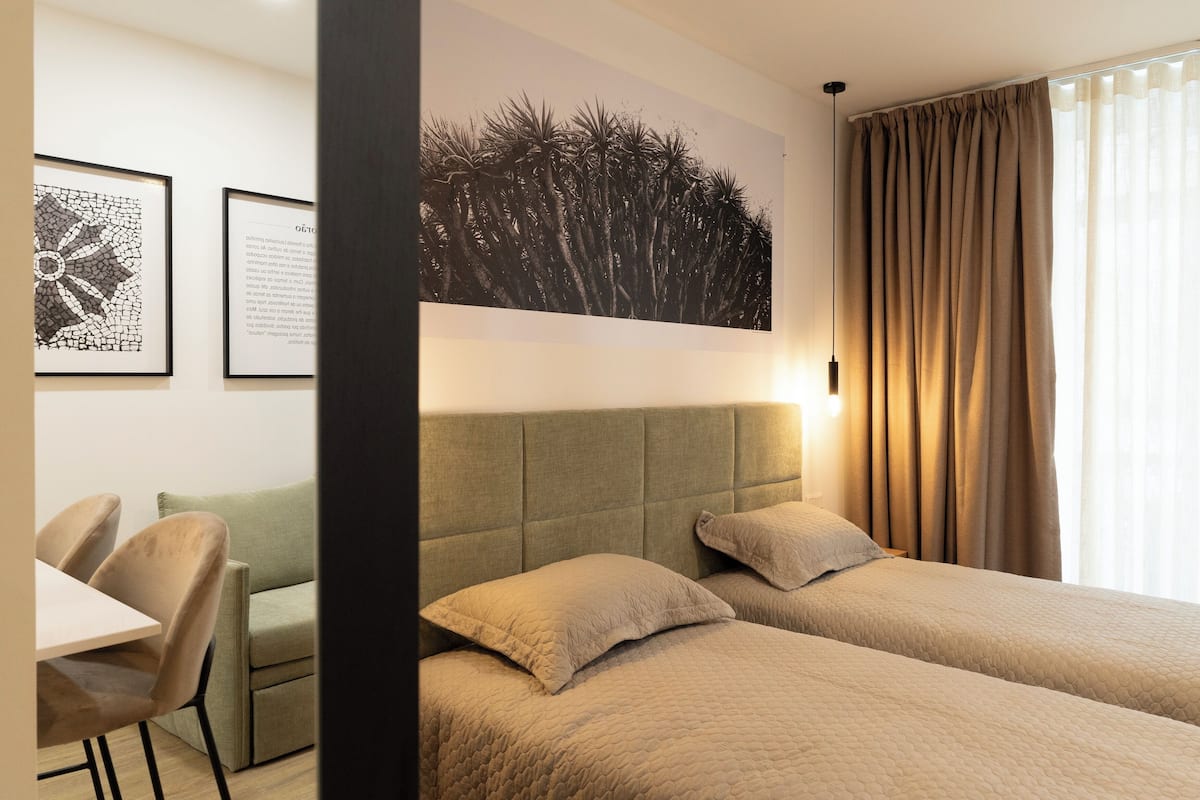 A hotel room with two beds, a sofa, a desk, and framed artwork on the wall.