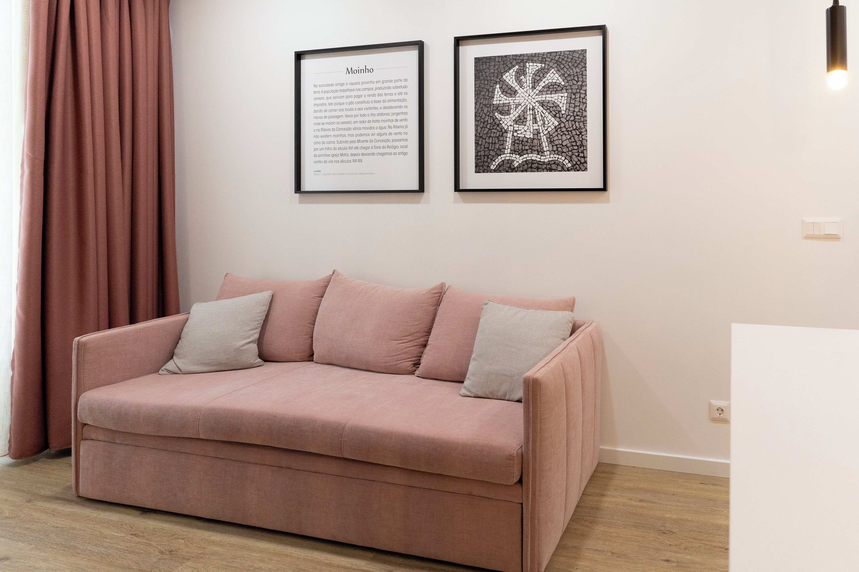 Un sofá rosa con almohadones, un documento de texto enmarcado y una obra de arte abstracta en la pared.