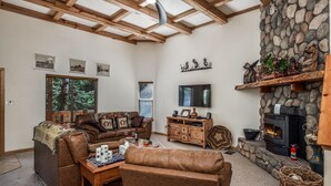 A cozy living room with a stone fireplace, wooden beams, and a television. - Woodlands Way Chalet- A cozy get-away in Cloudcroft NM.
 (Cloudcroft)