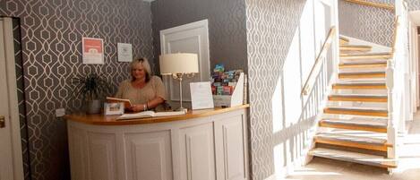 A reception desk with a woman standing behind it, a lamp, and a sign indicating a 45-minute check-in time.