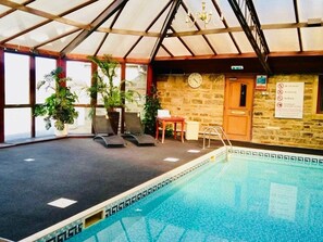 An indoor swimming pool with lounge chairs, a clock, and a sign indicating no lifeguard, no running, and no diving. - Leeming Wells  (Keighley)
