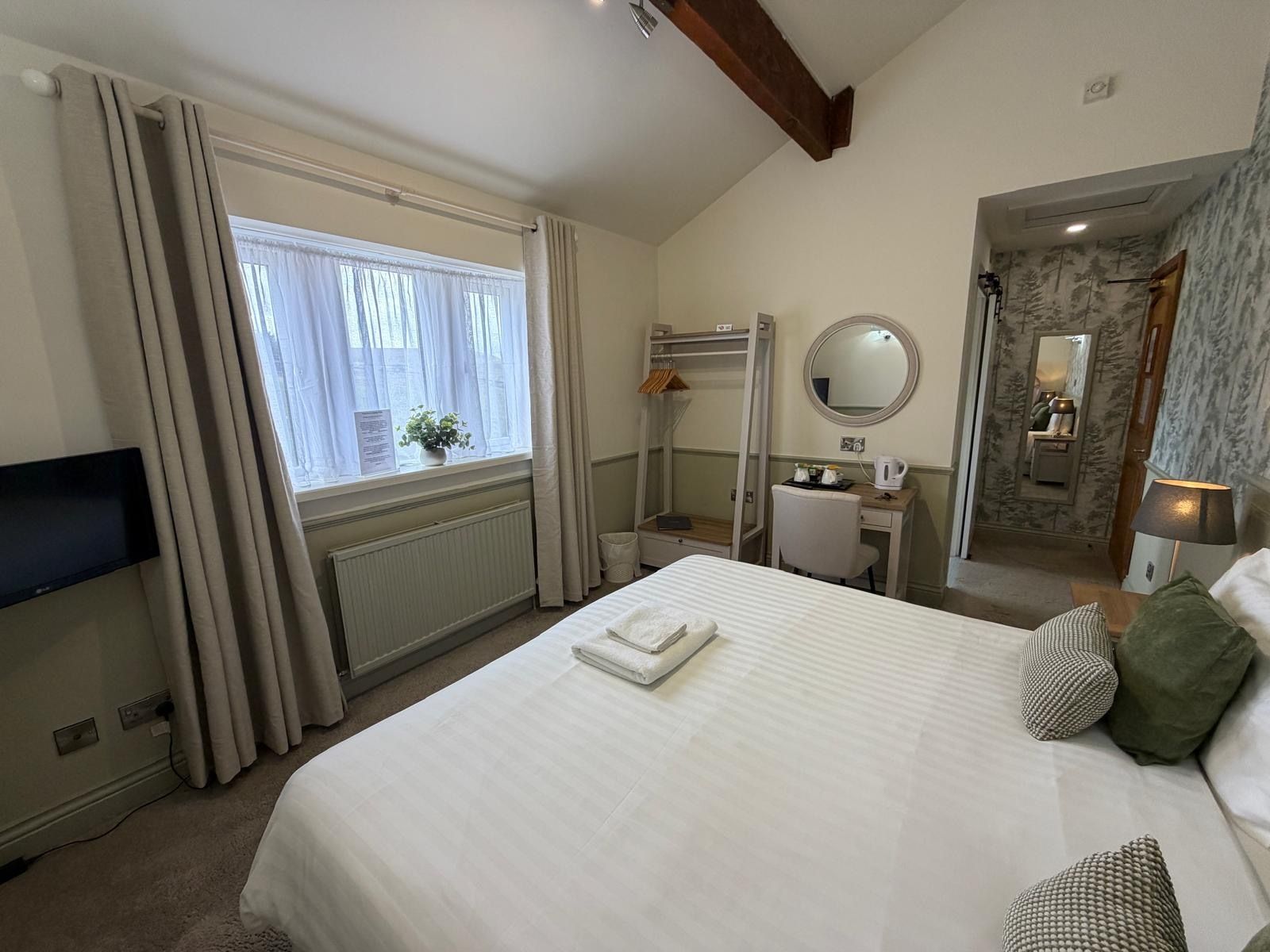 Habitación de hotel con cama, escritorio, espejo, radiador y televisor.