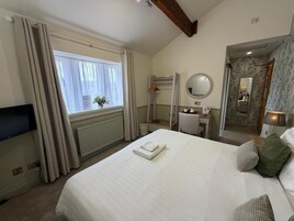 Habitación de hotel con cama, escritorio, espejo, radiador y televisor.