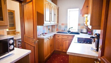 Una cocina compacta con armarios de madera, microondas, tostadora y lavamanos.