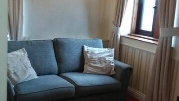Ein blaues Sofa mit zwei Kissen, ein Fenster mit Vorhängen und eine Heizung.