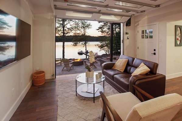 A modern living room with a glass door leading to a deck overlooking a lake.