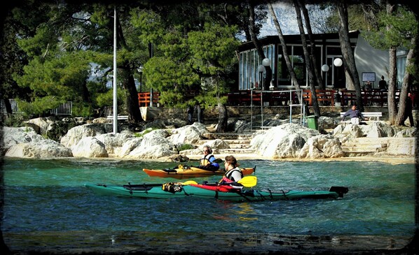 Una orilla con kayak, un edificio con balcón y un litoral rocoso.