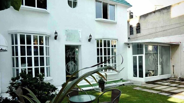 Un bâtiment blanc doté de grandes fenêtres et d’une porte en verre, une petite pelouse avec une table et des chaises, et une clôture blanche en bois.