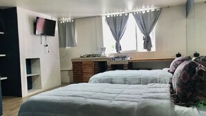 Une chambre à coucher avec un lit, un bureau, une télévision et une fenêtre avec des rideaux.