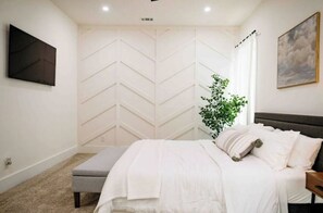 Relax in a serene bedroom with a large bed, wall-mounted TV, and chevron-patterned accent wall.