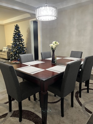 Un salón de conferencias con una mesa de madera oscura, sillas tapizadas en gris, un jarrón con flores blancas y una lámpara decorativa.