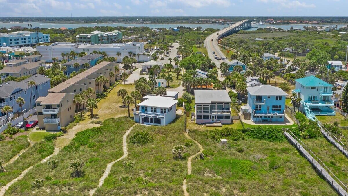 A coastal residential area with modern houses, a paved road, and a bridge in the background.