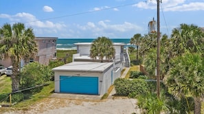 A coastal property with a blue garage, palm trees, and a view of the ocean. - Beachfront Apartment, Balcony & Sunrise Views (St. Augustine)