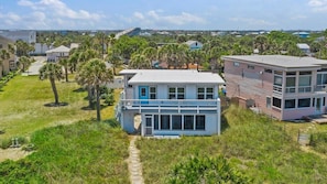 A two-story house with a large balcony, surrounded by a grassy yard and palm trees.