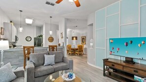 Una sala de estar con sofá, mesa de centro, televisor y decoración en la pared.