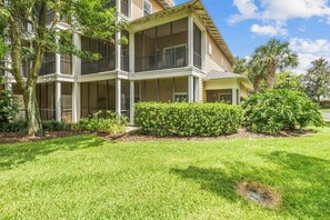 A multi-story building with balconies, a well-maintained lawn, and mature trees.