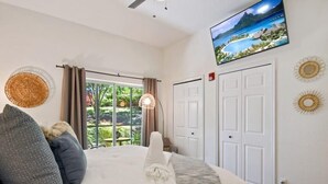 Un dormitorio con cama, televisor montado en la pared, una puerta y una ventana con cortinas.
