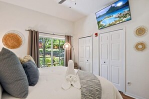 A bedroom with a bed, a television mounted on the wall, a door, and a window with curtains.
