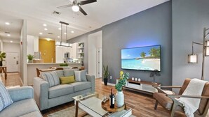 Una sala moderna con sofá, sillón, mesa de centro y televisor que muestra una escena de playa.