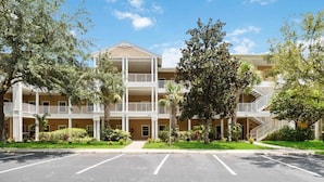 A multi-story hotel with balconies, a parking lot, and lush greenery.