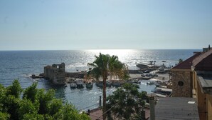 A coastal town with a historic stone building, boats docked at the harbor, and a palm tree in the foreground. - Casa del Porto Suite- Intimate private suite (Byblos)