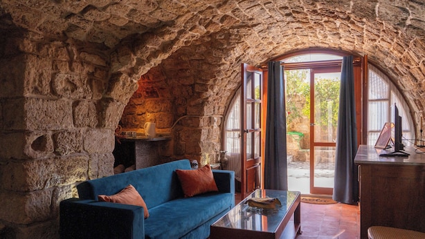 A stone-walled room with a blue sofa, a wooden table, and a view through an arched doorway. - Casa del Porto Suite- Intimate private suite (Byblos)