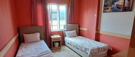 Una habitación con dos camas, una mesita, una ventana con cortinas y un cuadro en la pared.