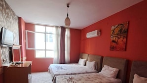 A hotel room with two beds, a television, a window with curtains, and a painting on the wall. - Savran Otel (Mersin)