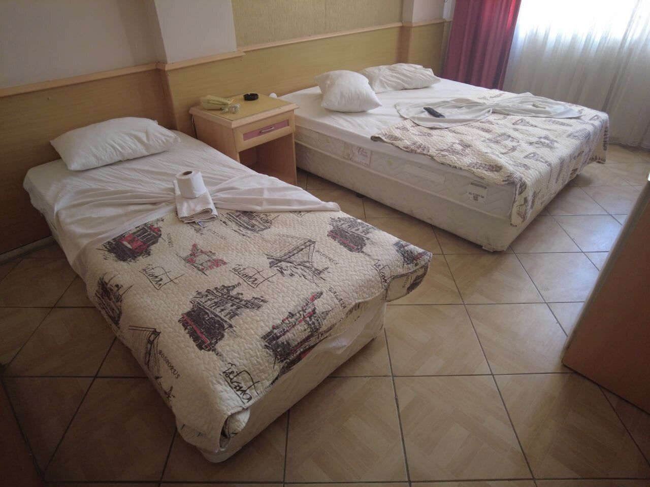 Two single beds with white linens, a wooden nightstand with a telephone and a lamp, and a patterned bedspread.