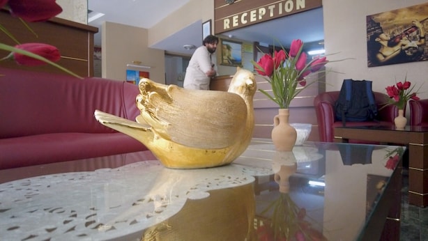 A reception area with a red sofa, a glass table with a decorative bowl, and a vase with flowers. - Savran Otel (Mersin)