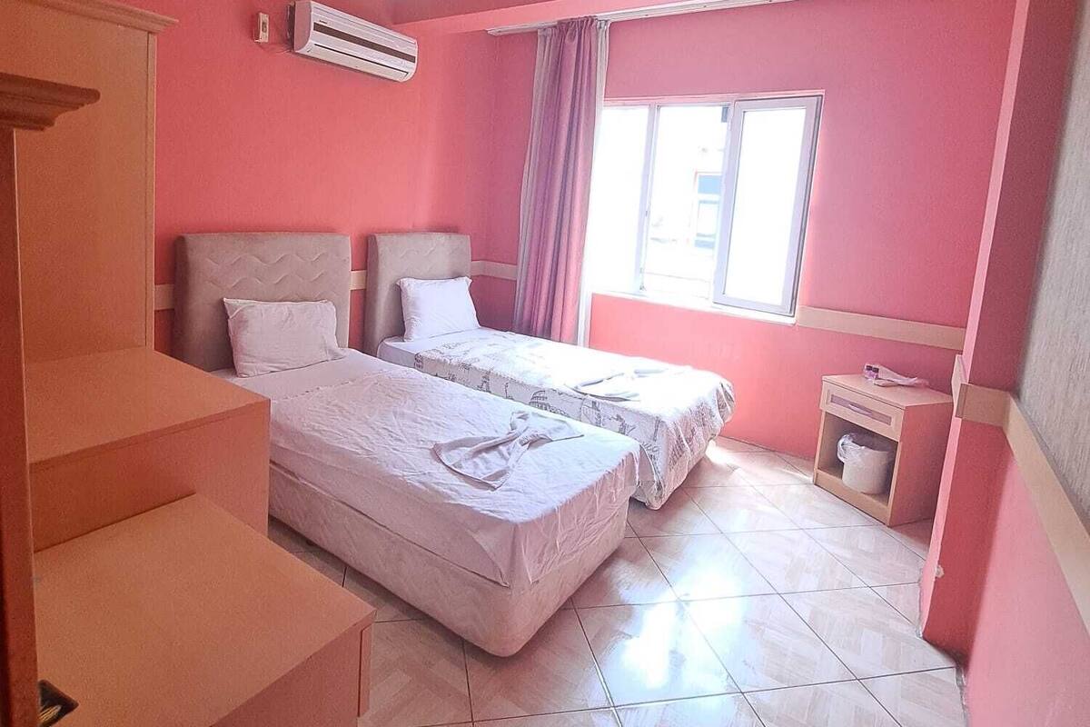 A room with two beds, a staircase, a window with curtains, and an air conditioning unit.