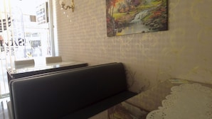 A restaurant interior with a booth seating area, a table with two chairs, and a wall-mounted painting of a landscape. - Savran Otel (Mersin)