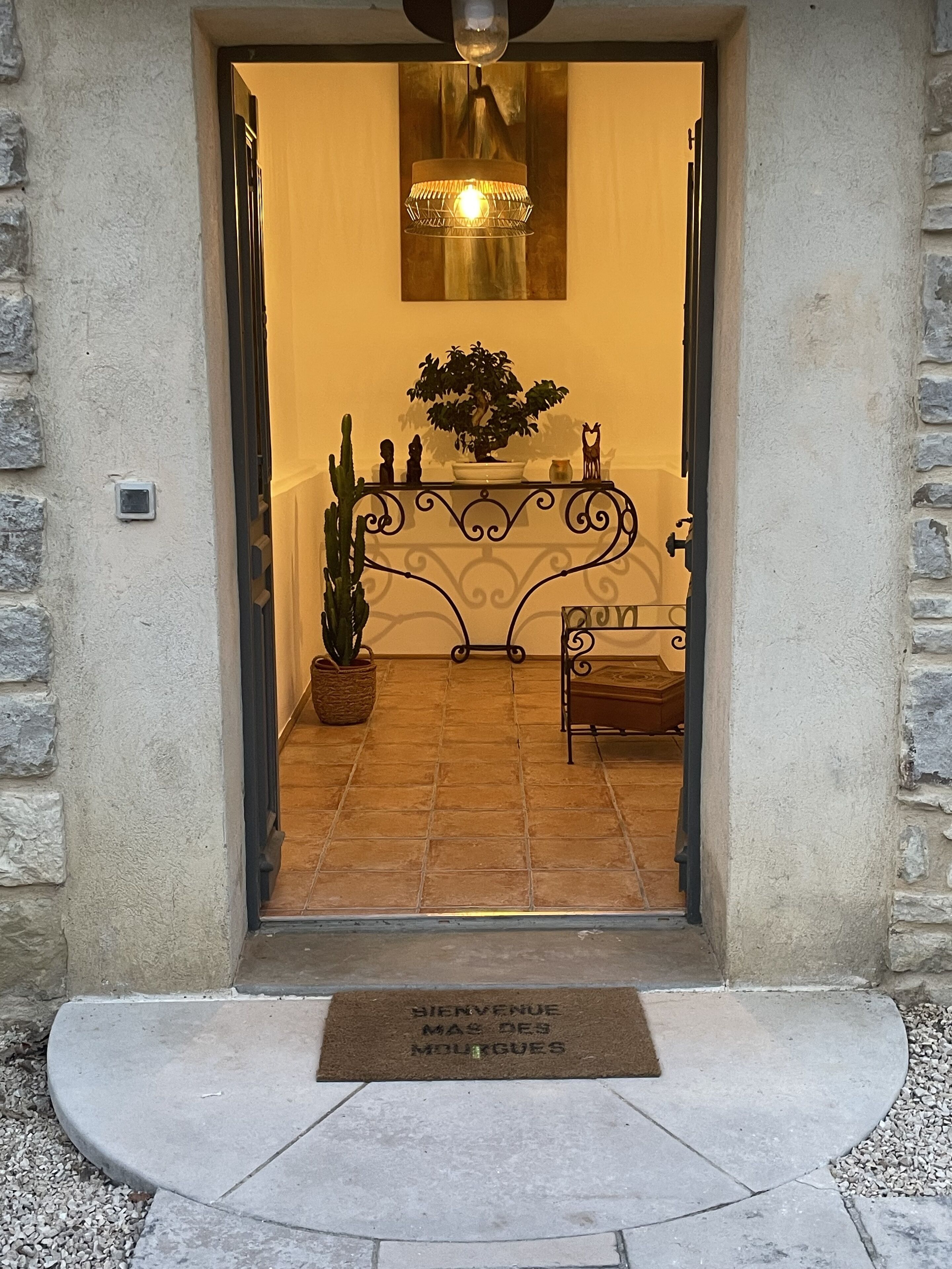 A hotel entrance with a wrought iron gate, a potted plant, a bench, and a welcome mat.