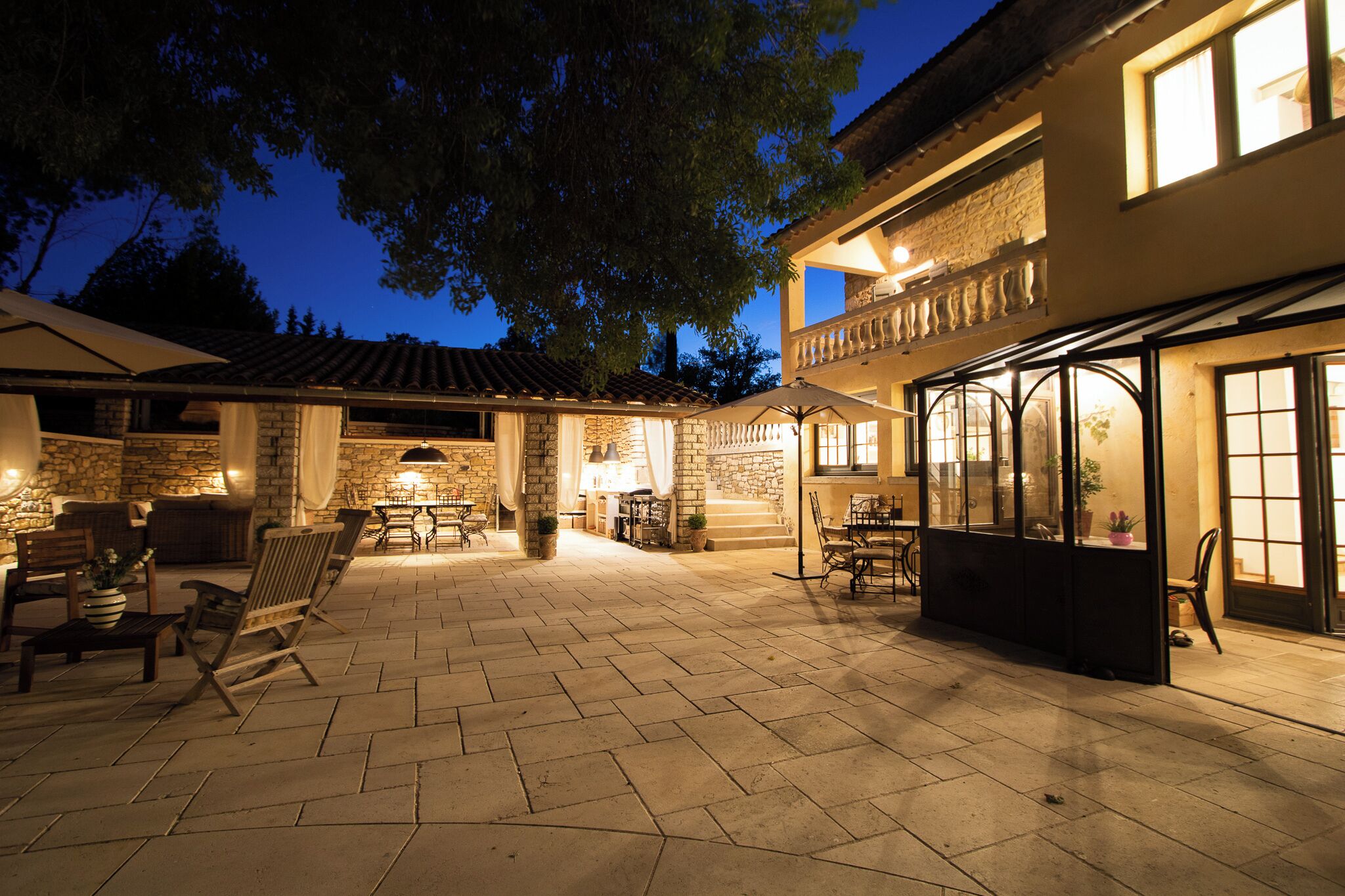 Un patio con suelo de piedra, mobiliario exterior y cerramiento de vidrio.