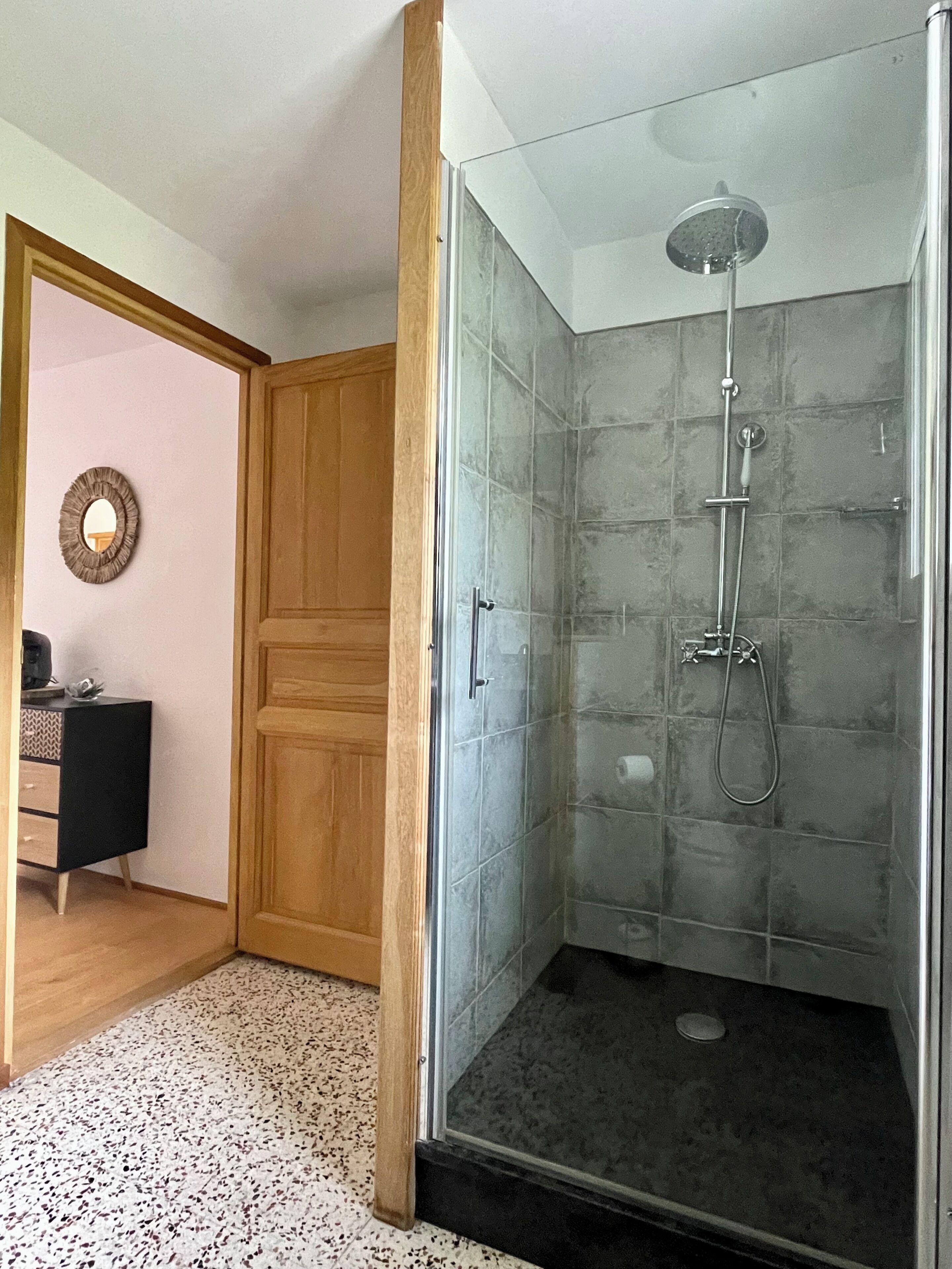 Une salle de bain moderne avec une douche à parois de verre, une porte en bois et un petit meuble-lavabo avec un miroir.